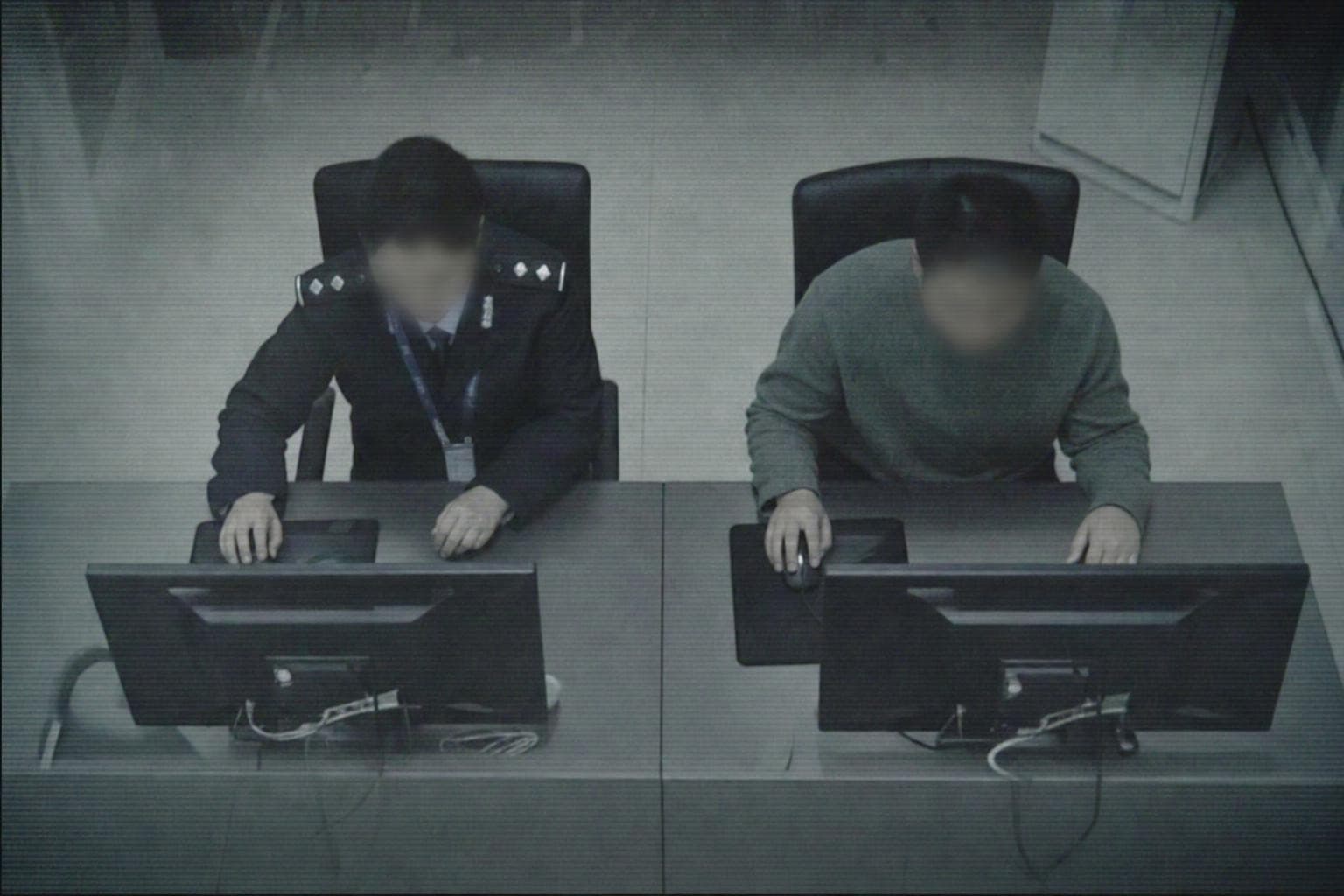 Two anonymous people seen from overhead surveillance at two identical screens comparing faces, one in a uniform with a lanyard, one in plain clothes, their work and their results indistinguishable from above.