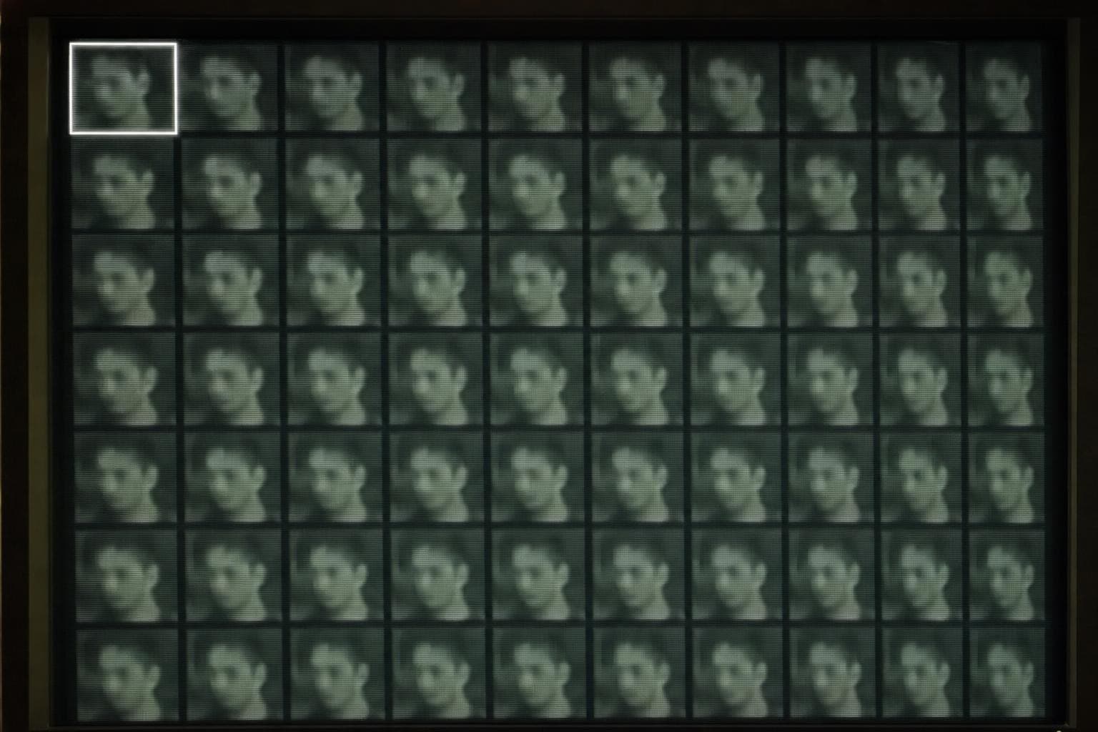 A ranked grid of near-identical anonymous CCTV faces on a screen, the top-left face boxed by a bright machine selection outline before any person has looked, the rest of the look-alikes left cold and unmarked.
