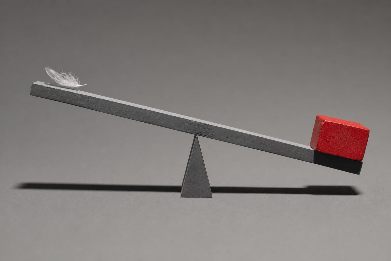 A plain matte-grey beam balanced across a single knife-edge fulcrum on a graphite surface; a small grey feather rests on the raised left end while a dense block of vermilion-red cast iron sits on the sunken right end, tipping the beam hard toward it, the iron block the only colour in the frame.
