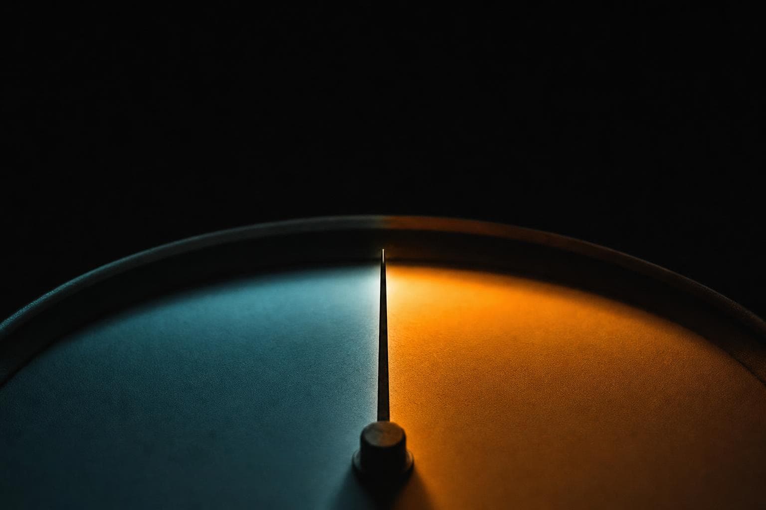 A precision analogue gauge whose slender needle rests dead centre at the exact tipping point between a teal-lit half of the dial and an amber-lit half.